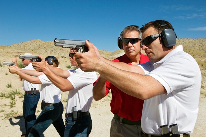 Instructor assisting men aiming hand guns at firing range